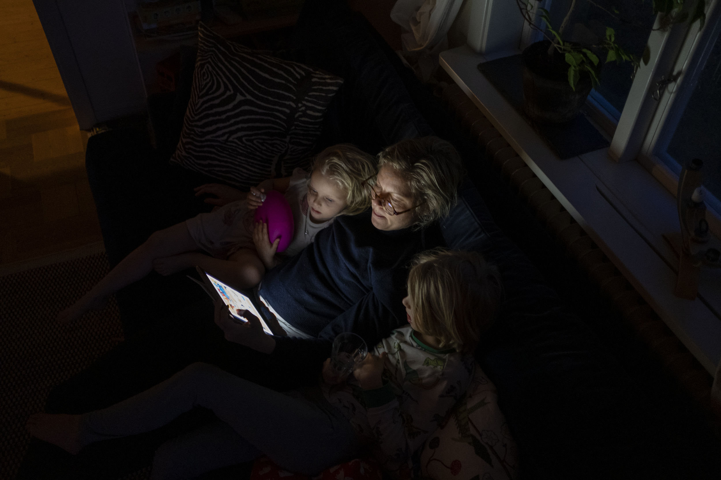 En kvinna läser för två barn i en soffa.